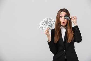 funny businesslady grimacing and holding cash and credit card in hands isolated over grey