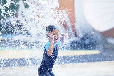 asian boy having fun with pool fountain shot during summer time
