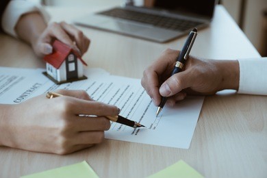 cropped image of real estate agent assisting client to sign contract paper at desk with house model