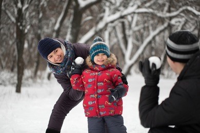 father, mother and son playing at snowballs in winter park
