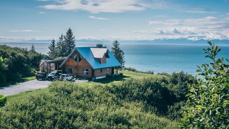 stunning landscape of a nice cabin in alaska overlooking the ocean from a green hill