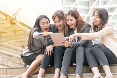 group of businesswoman sitting in the shade on the stairs,looking at digital tablet in a modern city. beautiful young woman wearing the business suit using tablet and laughing happily.