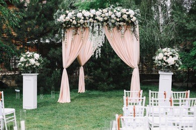 wedding arch decorated with flowers, white chairs and flowers bouquet