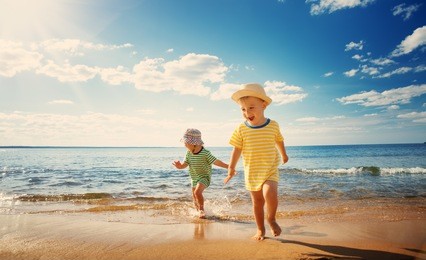 boy and girl playing on the beach on summer holidays. children in nature with beautiful sea, sand and blue sky. happy kids on vacations at seaside running in the water