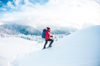 a man in snowshoes and trekking sticks in the mountains. winter trip. climbing of a climber against a beautiful sky with clouds. active lifestyle. climbing the mountain through the snow.