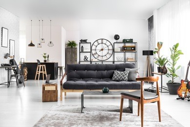 wooden chair next to table and dark settee in spacious apartment interior with guitar and plants. kitchen island in the background