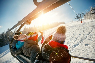 friends skiers and snowboarders on ski lift in the mountain at winter vacations back view