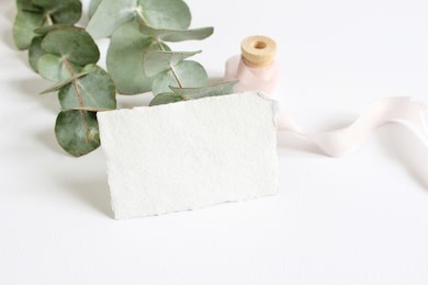 bright feminine spring stationery mockup scene with a handmade paper greeting card, spool of silk ribbon and eucalyptus leaves on a white table background. wedding styled stock photography.