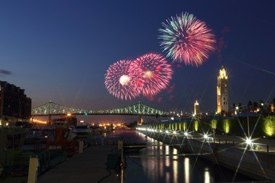 colorful fireworks explode over bridge. montreal clock tower at night. luminous colorful interactive jacques cartier bridge. old port montreal. reflection in water. montreal’s 375th anniversary. 