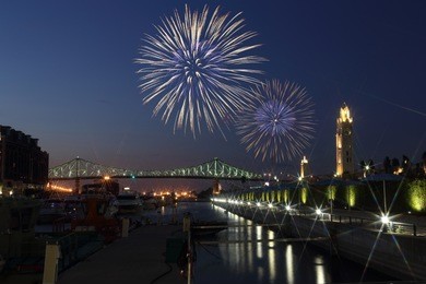 colorful fireworks explode over bridge. montreal clock tower at night. luminous colorful interactive jacques cartier bridge. old port montreal. reflection in water. montreal’s 375th anniversary. 