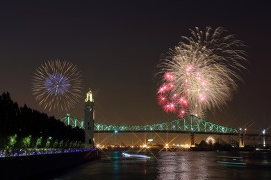 montreal clock tower at night. colorful fireworks explode over bridge, reflection in water. montreal’s 375th anniversary. luminous colorful interactive jacques cartier bridge. old port of montreal.