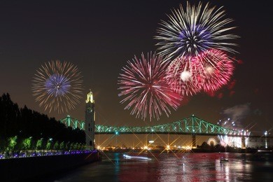montreal clock tower at night. colorful fireworks explode over bridge, reflection in water. montreal’s 375th anniversary. luminous colorful interactive jacques cartier bridge. old port of montreal.