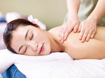 beautiful young asian woman lying on front on bed receiving massage in spa salon.