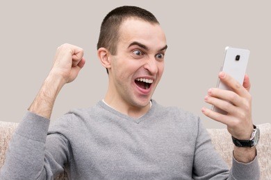 jubilant man looking at smart phone, sitting on the sofa, front view, isolated