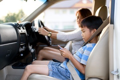 young asian boy using mobile phone in a care during travel with his mom.