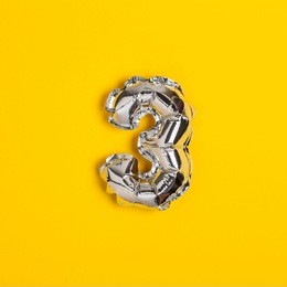 silver foil number 3 celebration balloon on a bright yellow background