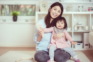 pretty japanese woman playing with her cute laughing baby girl on the floor at home