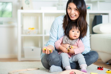 pretty japanese woman playing with her cute laughing baby girl on the floor at home