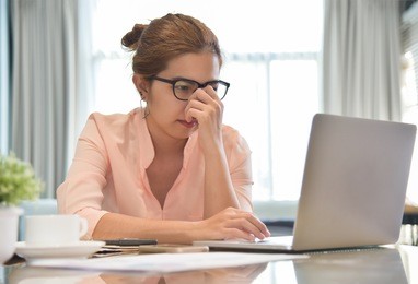 stressed young asian female creative designer wear glasses with a laptop computer having headache at her workplace. overwork. overtime.