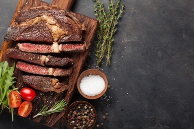 grilled ribeye beef steak with red wine, herbs and spices on a dark stone background. top view with copy space for your text