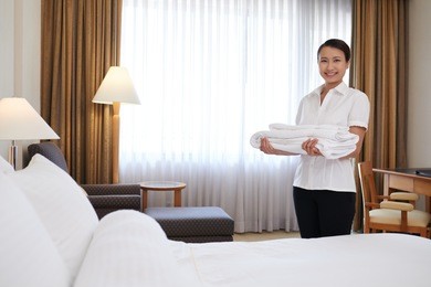 happy young asian chambermaid with a stack of fresh towels