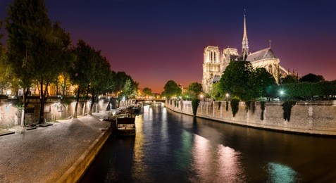 notre dame de paris with cruise ship on seine river at night in paris, france