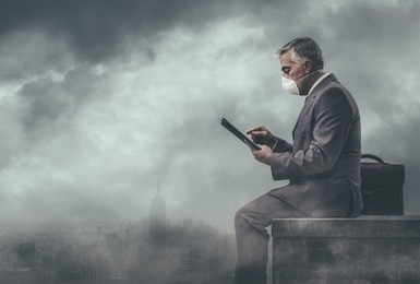 businessman sitting on a rooftop in a polluted city and using a tablet: environmental pollution and business concept