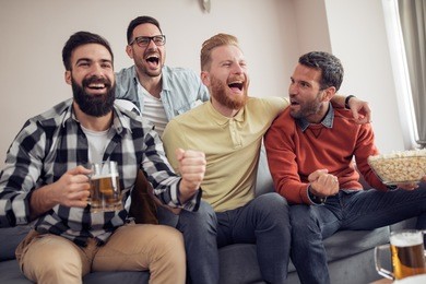 young football fans are drinking beer,cheering and smiling while watching football game at home.