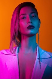 in the club concept. fashion portrait of rich glamourous woman wearing luxurious earrings, posing over orange background. pink, blue neon lights. close up. synthpop style. studio shot