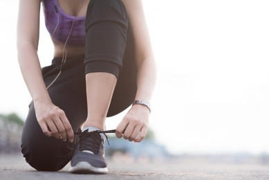 young woman runner tying shoelaces before jogging standing on footpath.