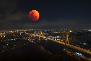 lunar eclipse, super blue blood moon taken from top of building on january31, 2018 with view of bhumibol bridge and curve of chao phraya river in bangkok.  (thai word on the bridge is the bridge name)