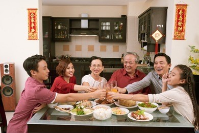 happy vietnamese family toasting with glasses of juice. scrolls wishing luck and wealth in the background