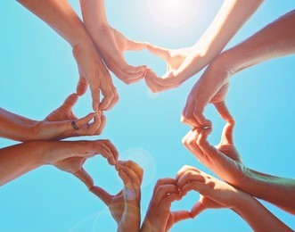 overhead view of a group of people making heart shapes with their hands directly below the sun with a lens flare toned with a retro vintage instagram filter 