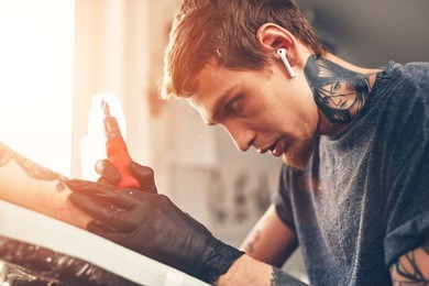a young guy, beats a tattoo on the hand of the girl in a tattoo parlor, rotary tattoo machine, black ink