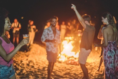 happy friends drinking beer at beach music festival - young people having fun summer vacation - youth lifestyle, holidays and party concept - soft focus on afro girl hand glass