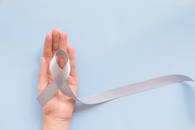parkinson's disease awareness or brain cancer grey bow or silver ribbon in woman or female hand over blue background with copy space for text, logo, wordings decoration, health medical concept