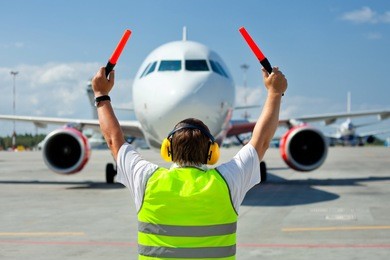 ground crew in the signal vest. aviation marshall / supervisor meets passenger airplane at the airport. aircraft is taxiing to the parking place.