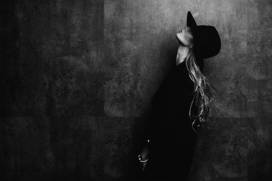 beautiful young mysterious blond girl in black hat and black jacket on gray background. eyes are covered with a hat. manicure - long red nails, nail polish. fashion, beauty.