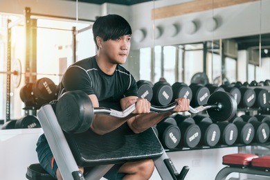 athletic young man working on his biceps by lifting a barbell in the gym