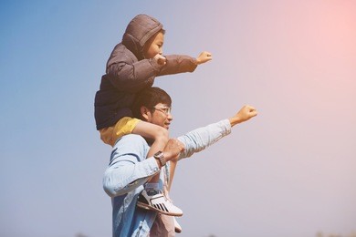 small boy is sitting on his father's shoulders in the field