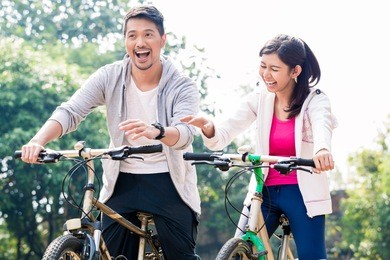 young asian couple laughing together while riding bicycles outdoors in summer 