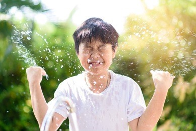 young asian boy wash his face by fresh water in a garden.