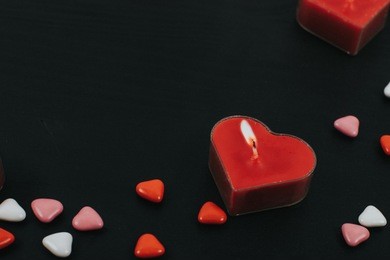 burning hearts shaped candles over black background. web banner for valentine's day. top view on composition with herts candles and candles. candy in the form of heart on black background 