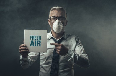 businessman wearing a mask and polluted air, he is holding a sign with fresh air advertisement