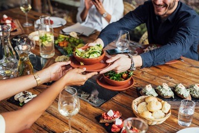 hands of cropped unrecognisable woman and man passing salad bowl at vegetarian restaurant.
