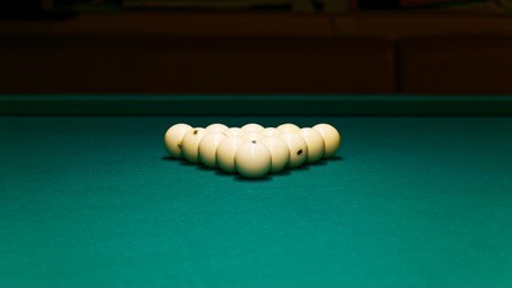 billiard balls in the form of a triangle on the green felt of a billiard table against dark background. shallow focus. copyspace.