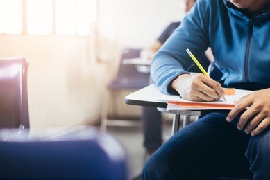 soft focus.high school or university student holding pencil writing on paper answer sheet.sitting on lecture chair taking final exam attending in examination room or classroom.student in uniform