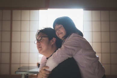 asian girl hugging her father from behind under sunlight