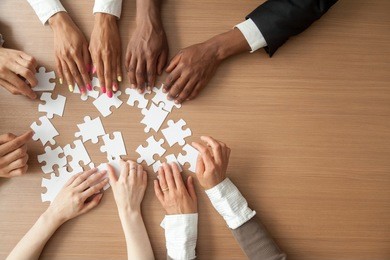 hands of multi-ethnic team assembling jigsaw puzzle, multiracial group of black and white people joining pieces at desk, successful teamwork concept, help and support in business, close up top view