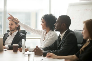 african woman raising hand to ask question at team training, curious black employee or conference seminar participant vote as volunteer at group office meeting with multiracial diverse businesspeople